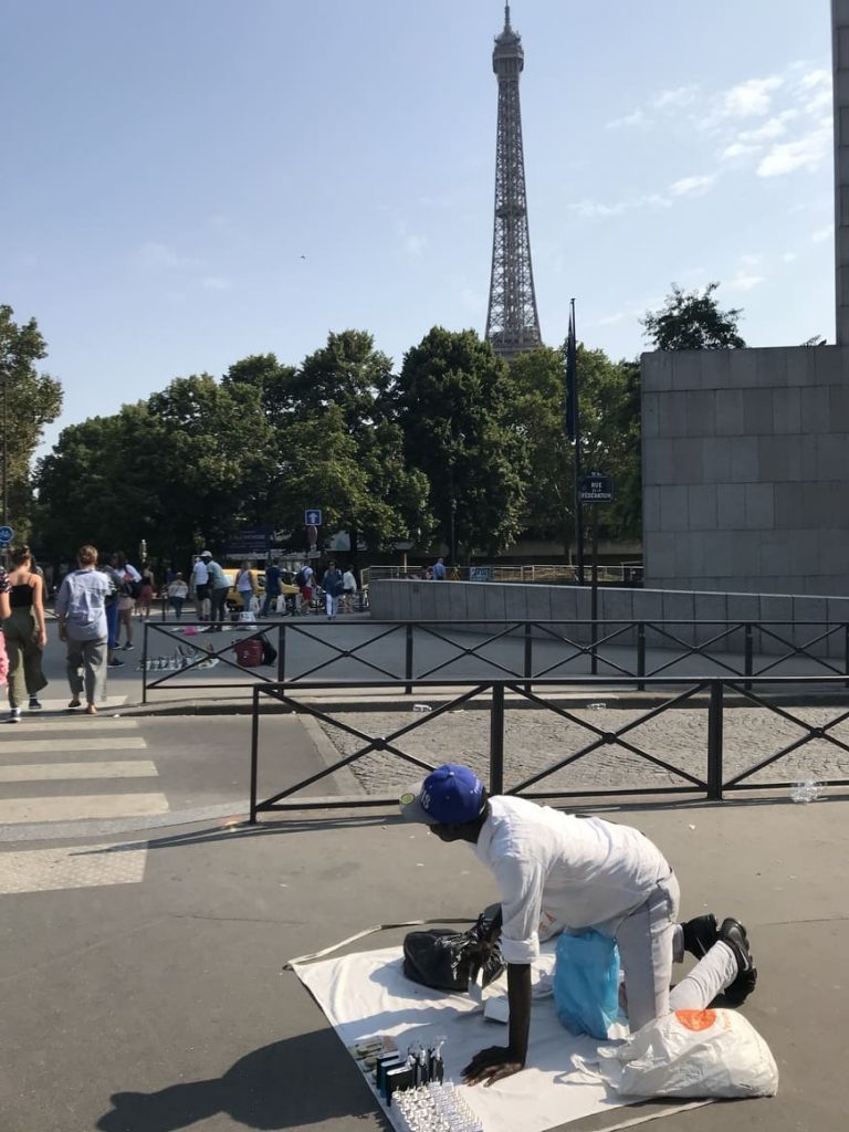 A street vendor in Paris, kneeling down in front of the Eiffel Tower