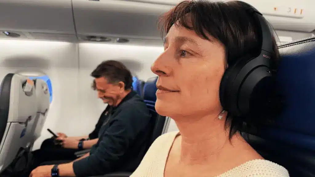 A woman wearing noice cancelling headphones to sleep on a plane