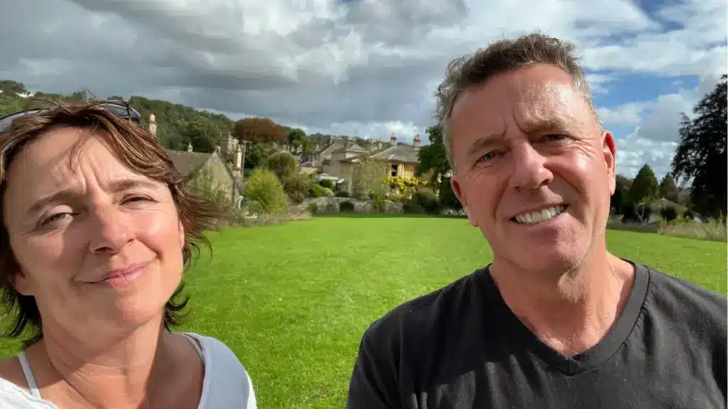 Married couple, husband and wife standing in a field in England talking about where is home on their podcast, It's a Drama!