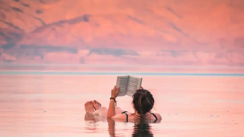 Woman laying in water reading a book. This is a post about the best books for women's book clubs