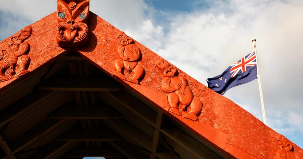 Māori Carving in front of a New Zealand flag.