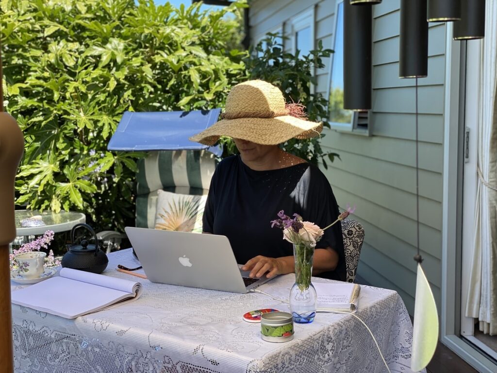 Woman in a hat. Writing a book outside in the garden on a computer